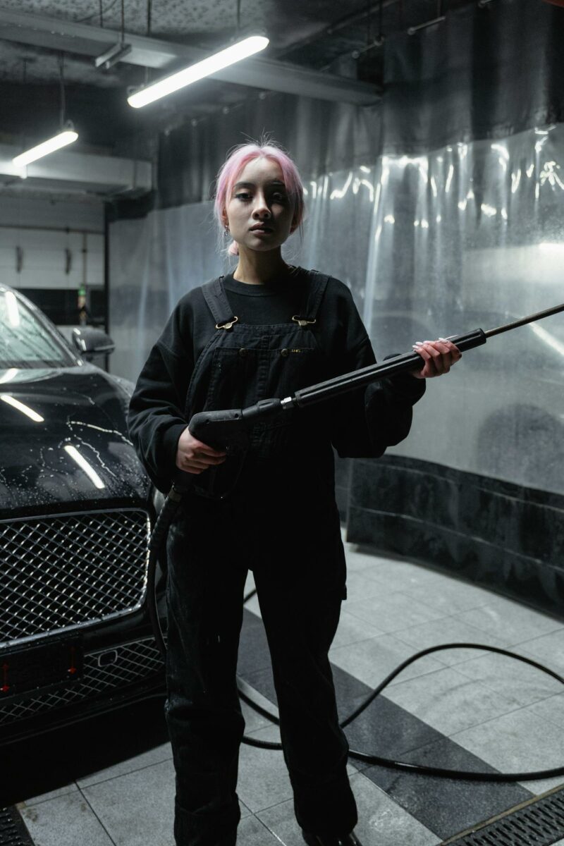 Young woman with spray gun cleaning a black car in an indoor car wash.